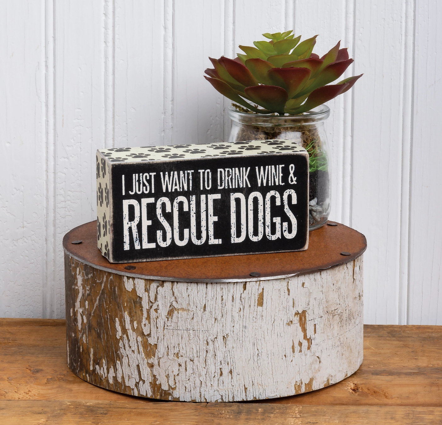 Decorative sign with text on a wooden block with a plant in the background.